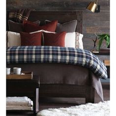 a bed with plaid sheets and pillows in a bedroom next to a wooden headboard