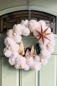 a christmas wreath with pom - poms hanging from the front door and a star on top