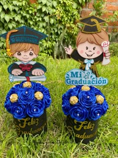 two graduation cupcakes sitting in the grass with blue flowers and decorations on them