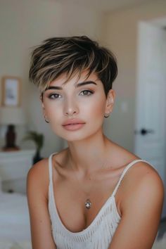 Person with short hair and hoop earrings sits in a softly lit room wearing a white top.