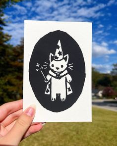 a hand holding up a black and white sticker with an image of a cat