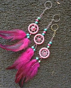 two pink dream catchers with beads and feathers hanging from hooks on a gray surface