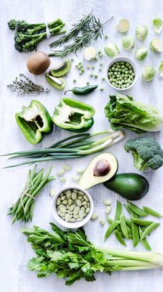 an assortment of vegetables are laid out on a white tablecloth, including broccoli, beans, and avocados