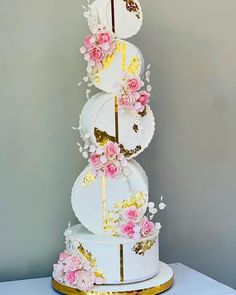 a three tiered white cake with pink flowers on top and gold trimmings