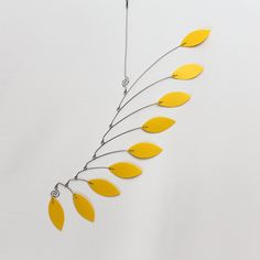 a metal sculpture with yellow leaves hanging from it's side on a white wall