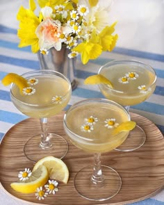 three glasses filled with lemonade sitting on top of a wooden tray next to flowers