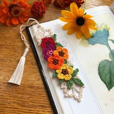 an open book with crocheted flowers and tassels on it next to a flower arrangement