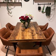 a wooden table with chairs around it and flowers in vases on the wall above