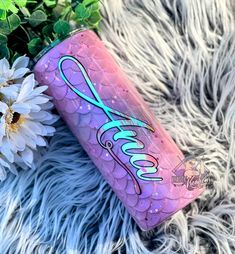 a pink and blue canister sitting on top of a furry surface next to flowers