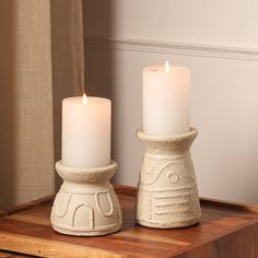 two white candles sitting on top of a wooden table