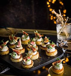 small appetizers are arranged on a black tray with lights in the back ground