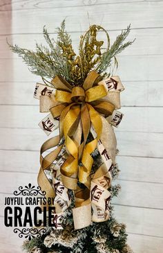 a christmas tree decorated with gold and brown ribbons on top of snow covered ground in front of white wood planks