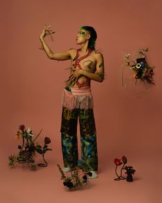 a man with tattoos standing in front of some plants and dead flowers on a pink background