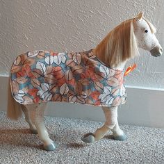 a toy horse wearing a blanket on top of it's head and legs in front of a wall