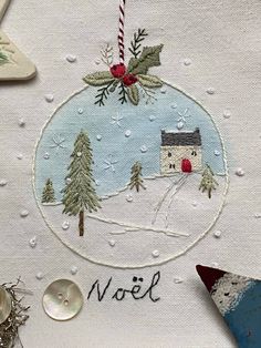 a christmas ornament with a house in the snow and holly decorations on it