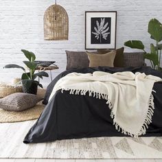 a bedroom with white brick walls and black bedding, plants on the side of the bed