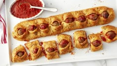 a white plate topped with pigs in a blanket next to a bowl of ketchup