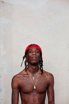 a man with tattoos on his chest standing in front of a white wall and wearing a red bandana