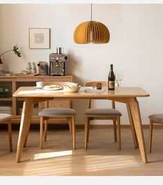 a wooden table with two chairs and a wine bottle on it in front of a white wall