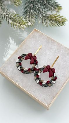 a pair of earrings sitting on top of a white box next to a christmas tree