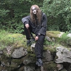 a man with long hair and makeup sitting on rocks