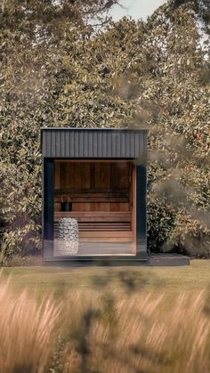 an outdoor sauna in the middle of a field with tall grass and trees behind it