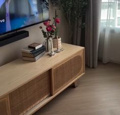 a flat screen tv sitting on top of a wooden entertainment center next to a window