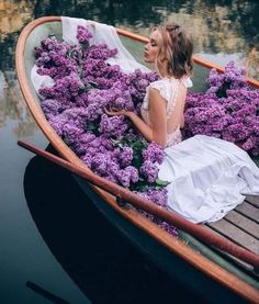 a woman in a white dress is sitting in a boat with purple flowers on the water