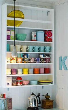 the shelves in the kitchen are filled with colorful dishes and coffee mugs on them