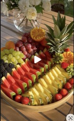 a bowl filled with lots of fruit on top of a wooden table next to flowers