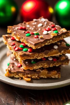 three pieces of chocolate and sprinkles on a plate with christmas ornaments in the background