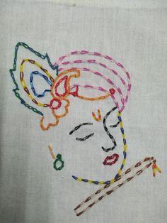 a woman's face is embroidered on a white linen piece with colorful threads