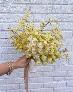 a person holding a bouquet of flowers in front of a white brick wall with gold bracelets