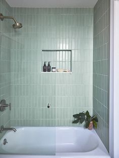 a white bath tub sitting under a window next to a green tiled wall and floor