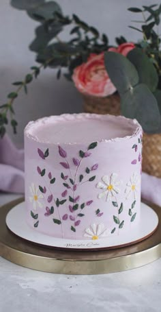 a pink cake decorated with flowers and leaves on a gold platter next to a potted plant