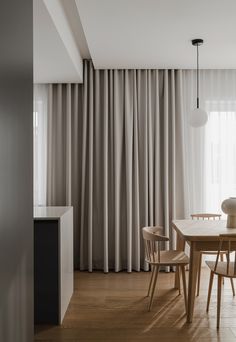 a dining table and chairs in front of a curtained window