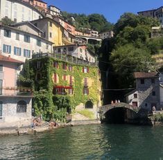 some people are sitting on the side of a building by the water and there is a bridge in front of them