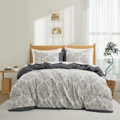 a bed with white and grey comforters in a room next to a window,