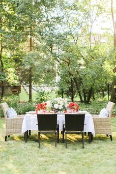 an outdoor dining table set with four chairs and two vases filled with red flowers