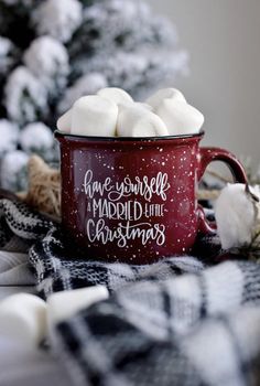 a red mug filled with marshmallows sitting on top of a plaid blanket