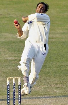 a man in white uniform playing a game of cricket on grass with two red balls