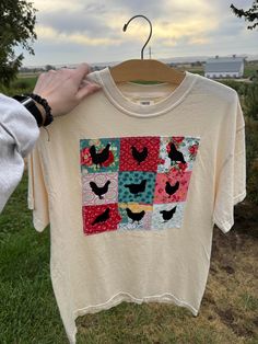 a person holding up a t - shirt with birds on it in front of some grass