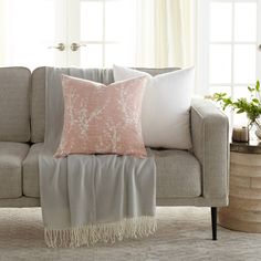 a living room with a gray couch, pink and white throw pillow and some plants