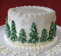 a white frosted cake decorated with trees and snowflakes on it's side