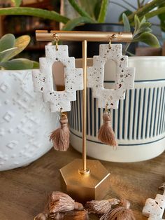 a pair of earrings with tassels hanging from them on a stand next to potted plants