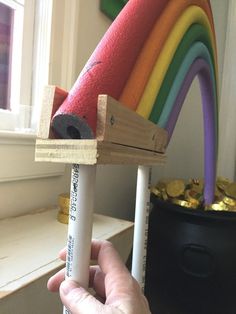 a hand holding a wooden toy with a rainbow in the background and a window behind it