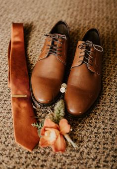 a pair of brown shoes next to a tie and flower