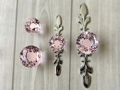 three pieces of jewelry sitting on top of a wooden table with pink stones and leaves