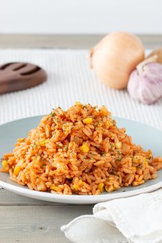 a white plate topped with rice and vegetables next to garlic on a wooden tablecloth