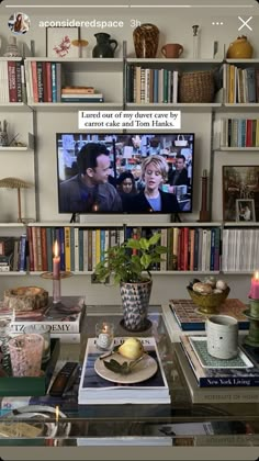 a television sitting on top of a book shelf next to a vase filled with flowers